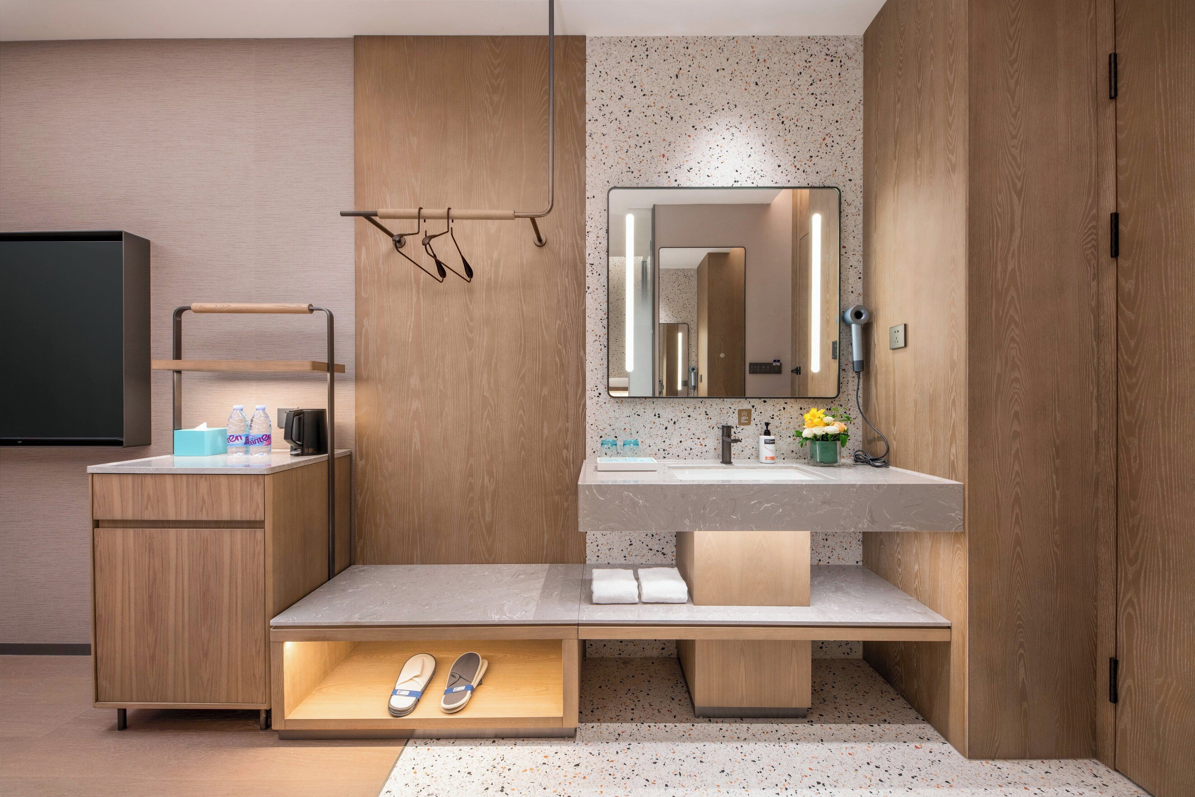 A modern bathroom with a wooden vanity, a mirror, and a built-in shoe storage.