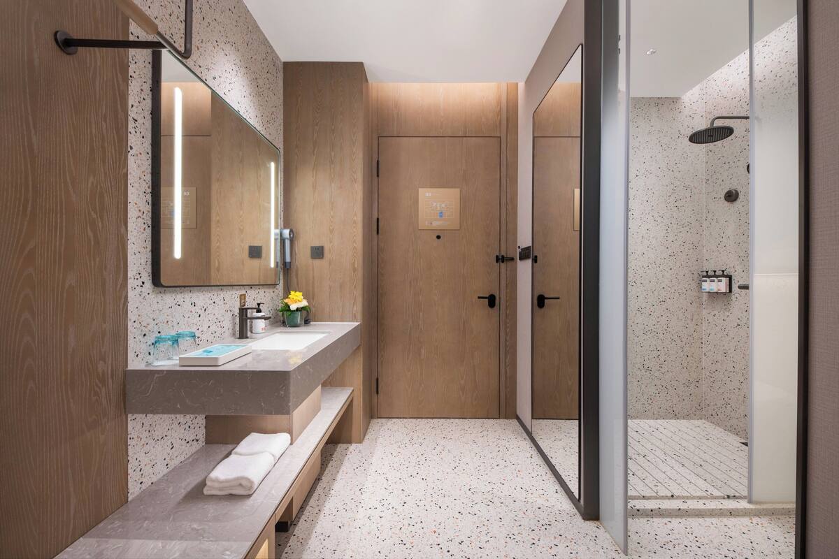 Un baño moderno con tocador de madera, cabina de ducha con mampara de vidrio y panel de control a la vista.