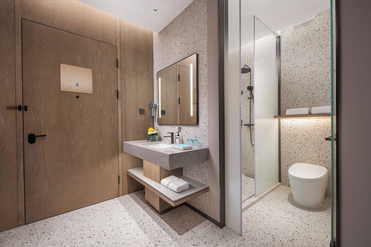 A modern bathroom with a wooden door, a large mirror, a sink with a towel shelf, and a toilet.