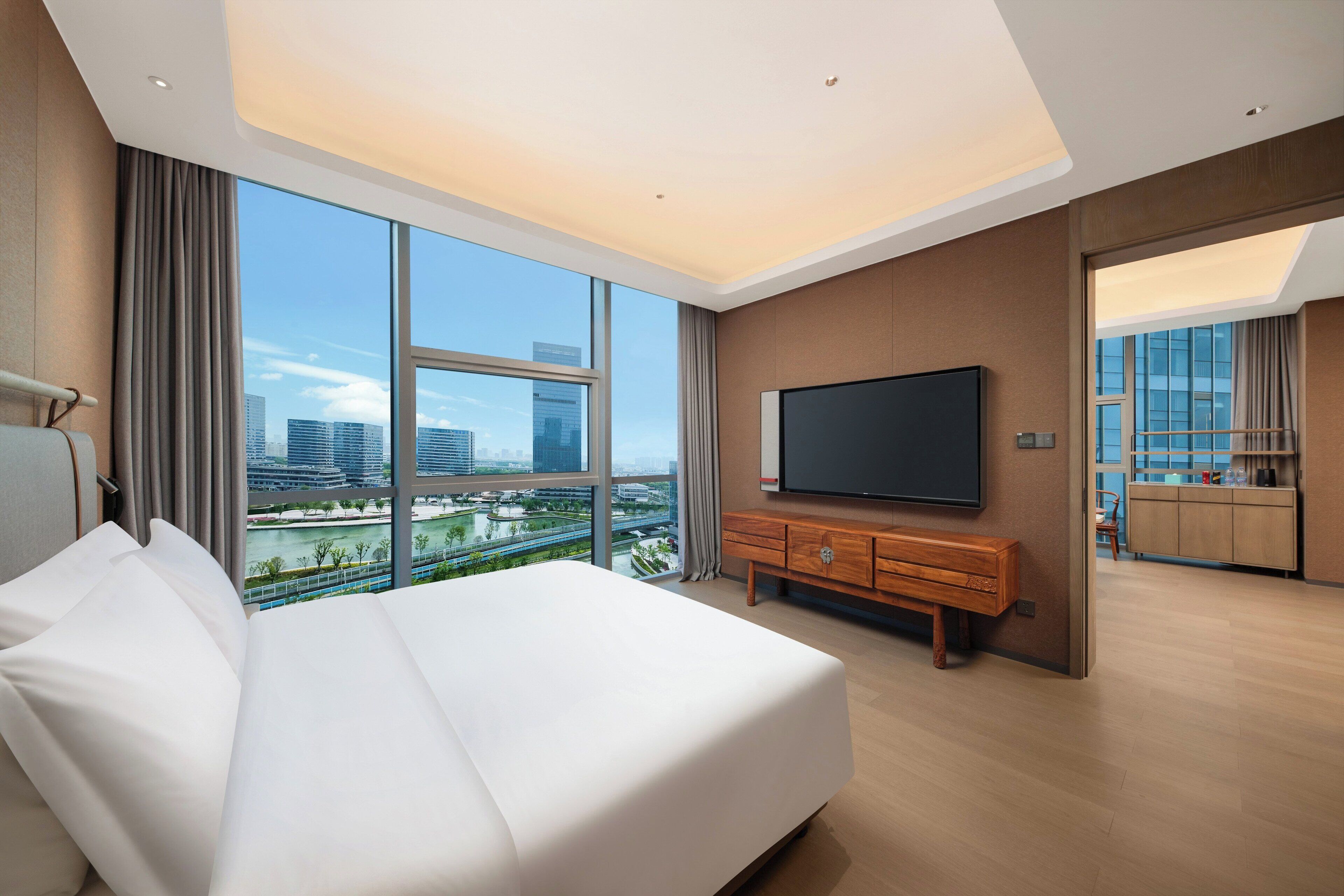 A modern hotel room with a large bed, a flat-screen TV, and a city view.