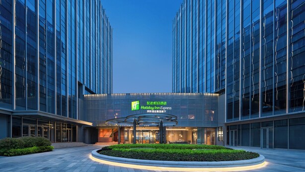 A modern Holiday Inn Express building with a glass facade, a well-lit entrance, and a landscaped area in front. - Holiday Inn Express Suzhou North Station by IHG (Suzhou)