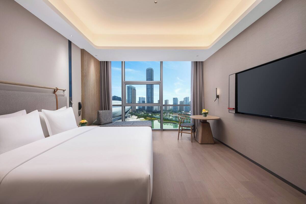 Habitación de hotel moderna con una cama grande, un escritorio y vistas a la ciudad.