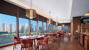 A modern dining area with wooden tables and chairs, large windows with a city view, and hanging pendant lights. - Holiday Inn Express Suzhou North Station by IHG (Suzhou)