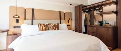 A hotel room with a large bed, a wooden wardrobe, a nightstand, and a wall-mounted lamp.
