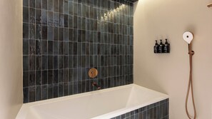 A bathroom with a bathtub, a shower, and a wall-mounted shelf with bottles. - Hotel Indigo Gandia Beach by IHG (Gandia)