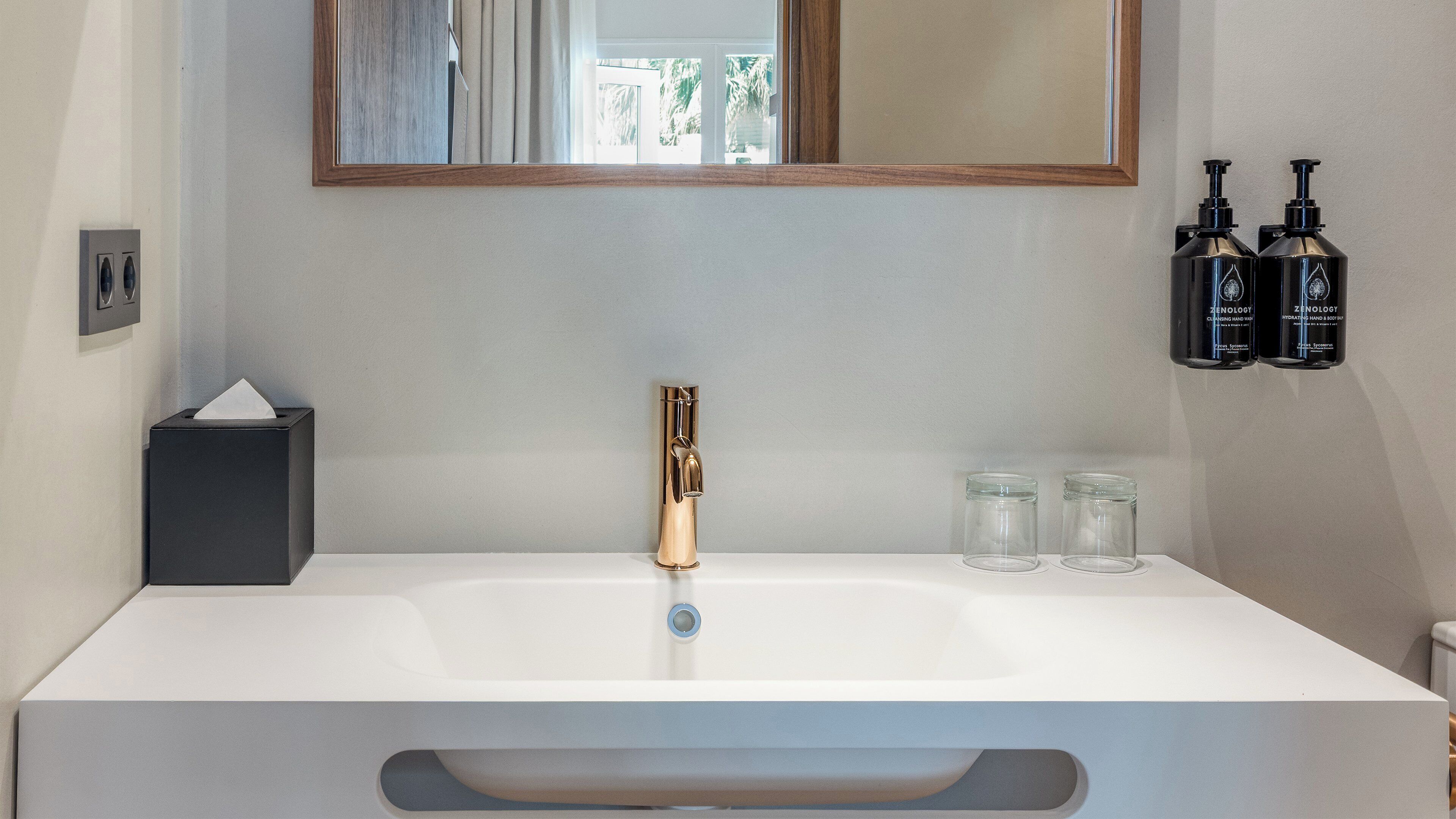 A bathroom with a white sink, gold faucet, and two black bottles of hand soap.