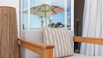 A modern living room with a sofa, a patterned throw pillow, a wooden side table, and a large window with an umbrella outside.