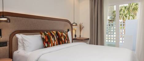 A hotel room with a bed, a nightstand, a lamp, and a view of palm trees through the window.