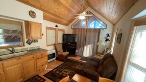 A cozy living room with a fireplace, a dining area with a table and chairs, a kitchen with wooden cabinets, and a ceiling fan. - Cabin #5 at Hyatt Lake Resort (Jackson County)