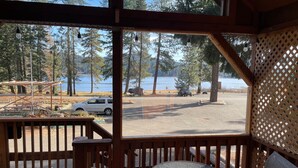 A wooden deck with a glass table and chairs, overlooking a parking area and a lake with trees. - Cabin #5 at Hyatt Lake Resort (Jackson County)