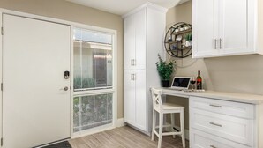 A kitchen with white cabinetry, a dining area with a white chair, and a small table with a laptop and wine bottle.