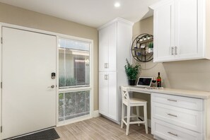 A kitchen with white cabinetry, a dining area with a white chair, and a small table with a laptop and wine bottle.