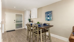 A dining area with a table set for four, a white door, and a painting on the wall.