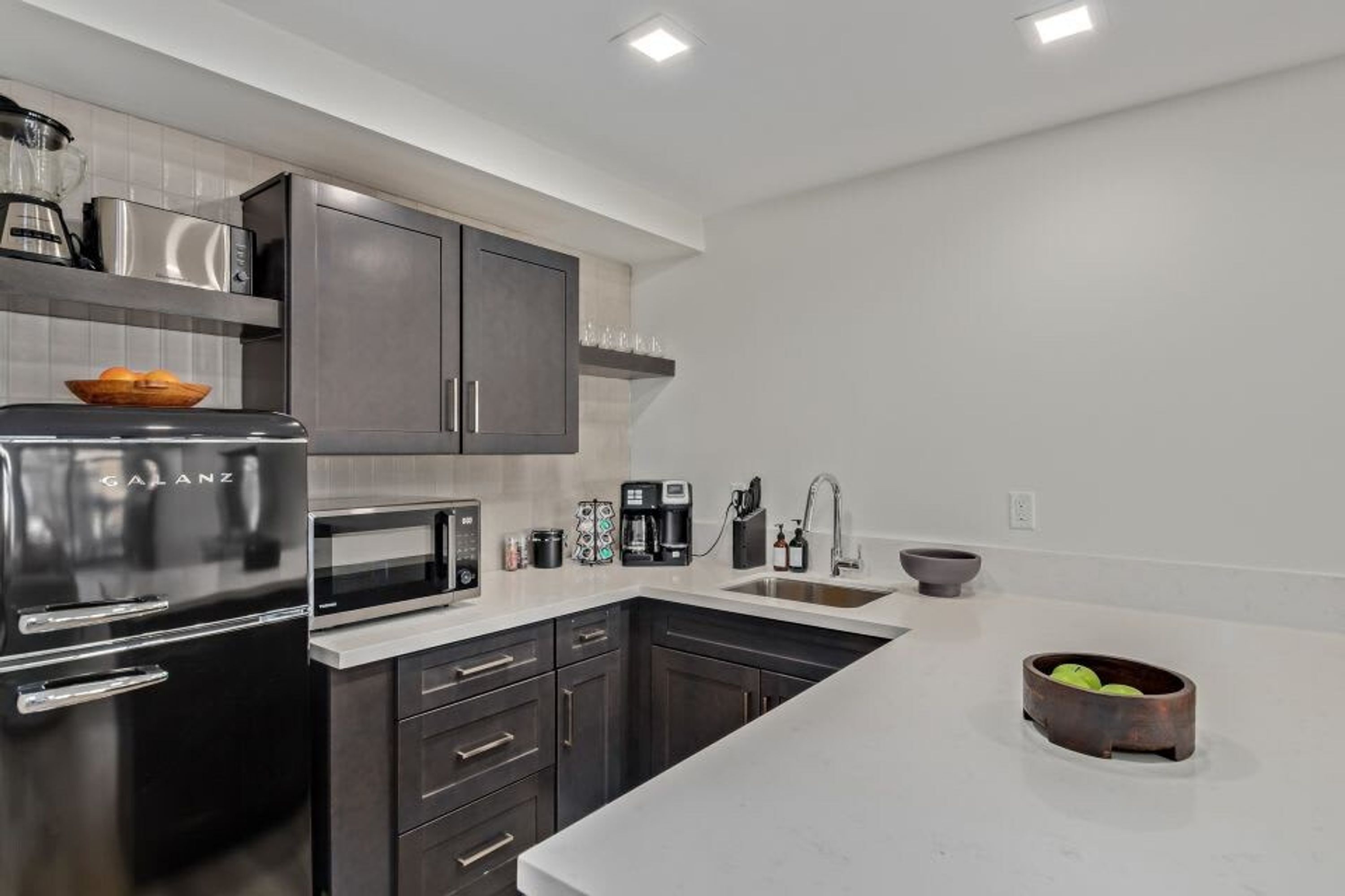 A modern kitchen with dark cabinets, a stainless steel refrigerator, a microwave, and a coffee maker.