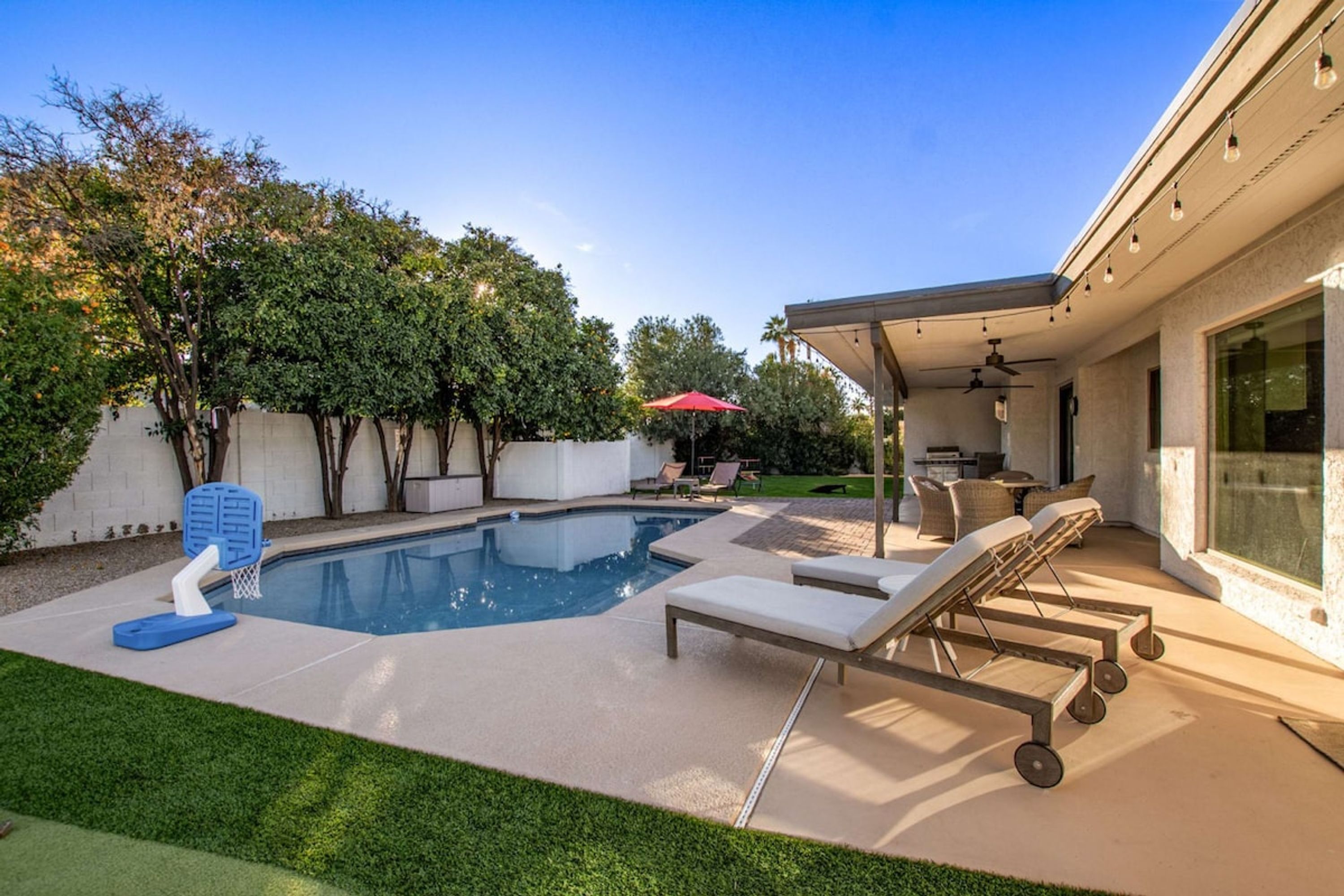 A backyard with a swimming pool, lounge chairs, and a covered patio area.