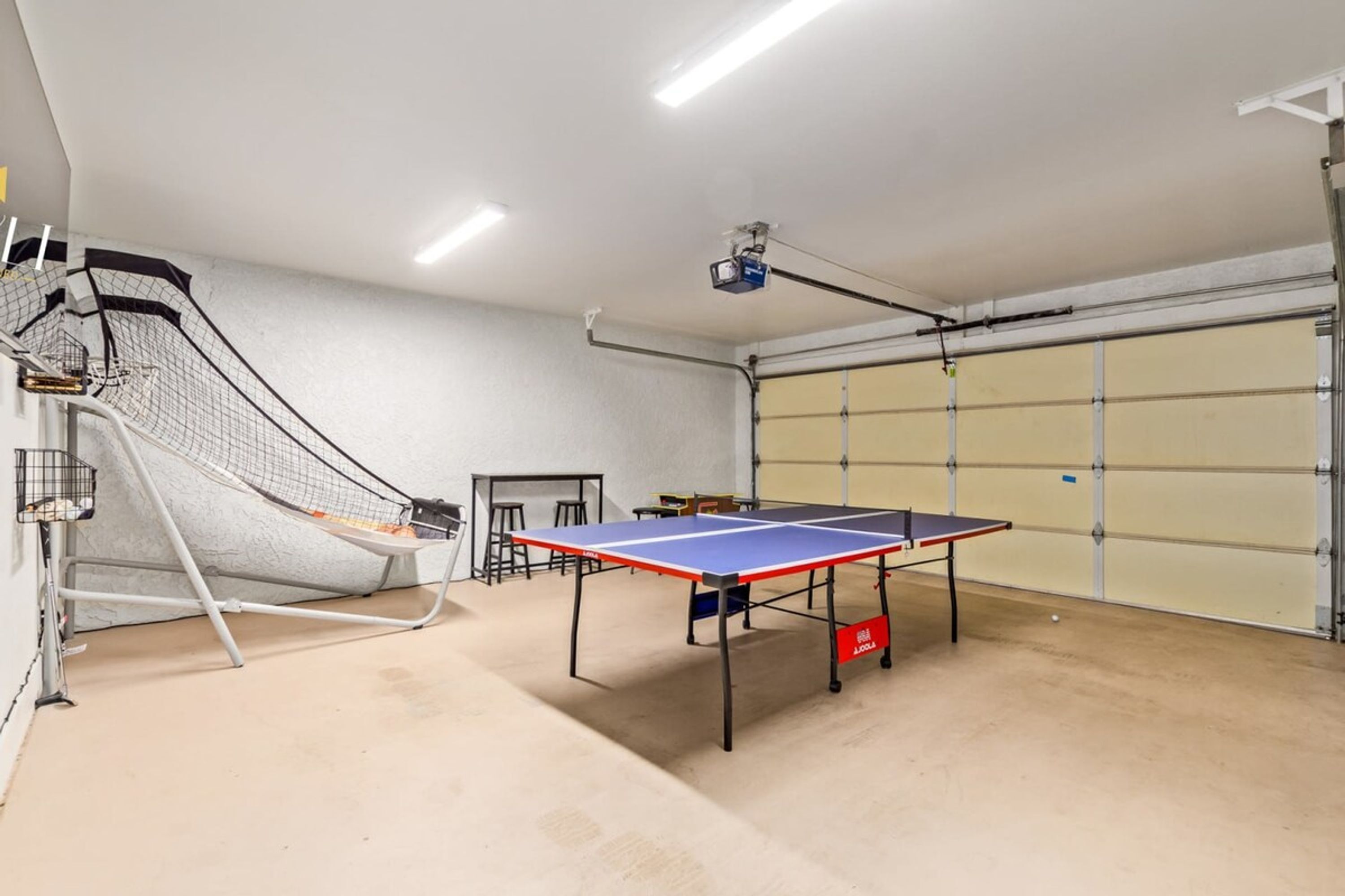 A ping pong table, a small table, and a netted area in a garage.