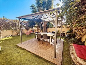 Un patio exterior con terraza de madera, zona de estar cubierta y una parrilla para barbacoa.