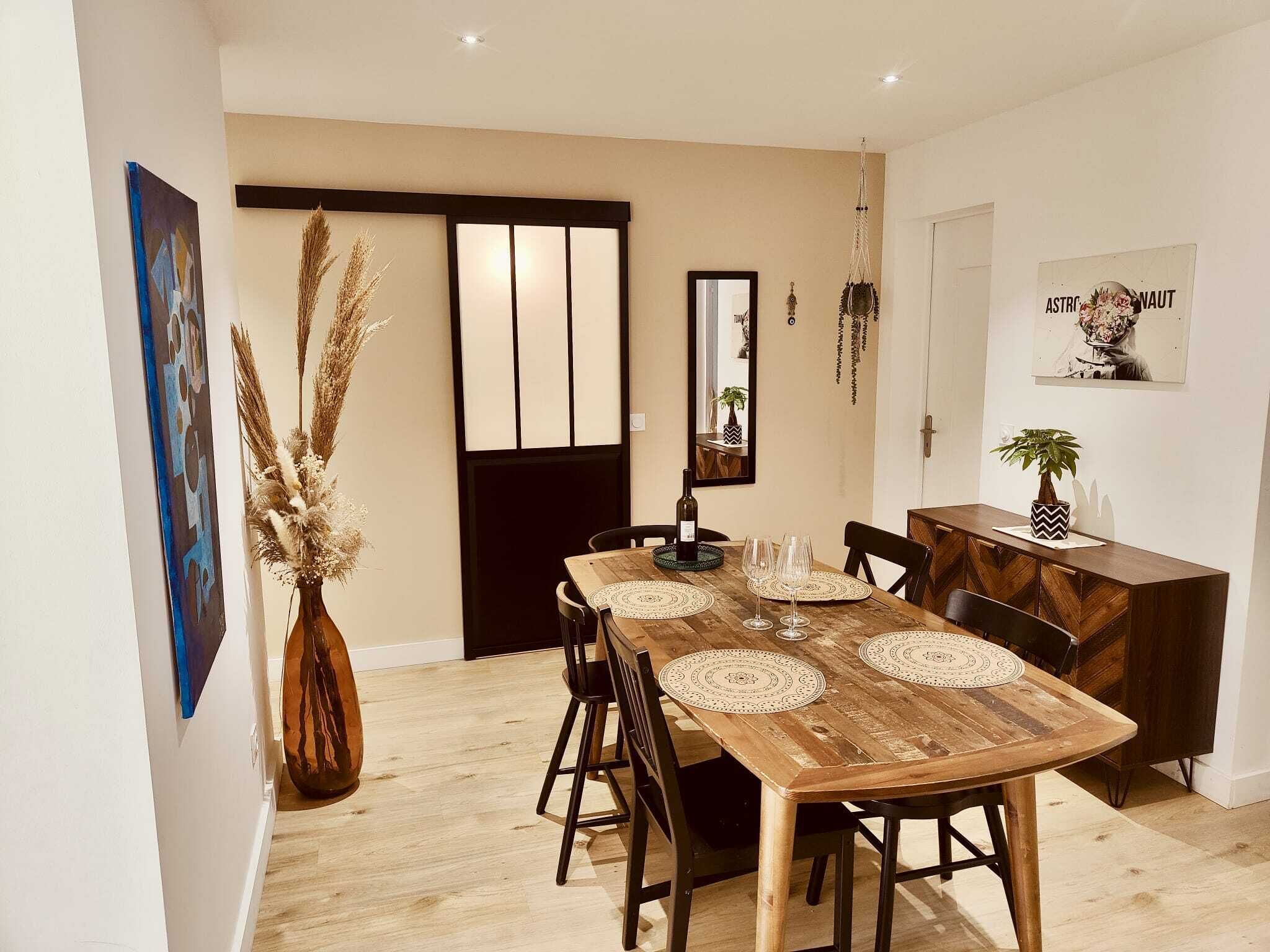 Un comedor con una mesa de madera, sillas y elementos decorativos como un jarrón con plumas de pájaro y un adorno colgante.