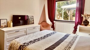 Un dormitorio con cama, televisor, cómoda y ventana con cortinas.