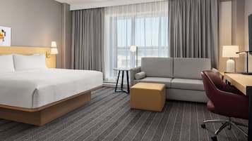 A hotel room with a bed, a sofa, a desk, and a chair.
