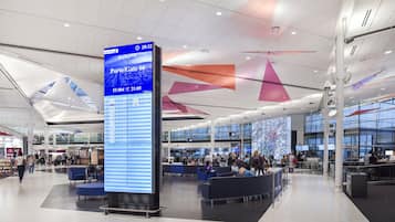 Un moderno terminal de aeropuerto con un panel informativo digital de vuelos, zonas de descanso y un amplio muro de cristal.