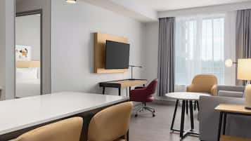 Una habitación de hotel moderna con una cama grande, un escritorio, un televisor y una zona de estar con sillas y una mesa.