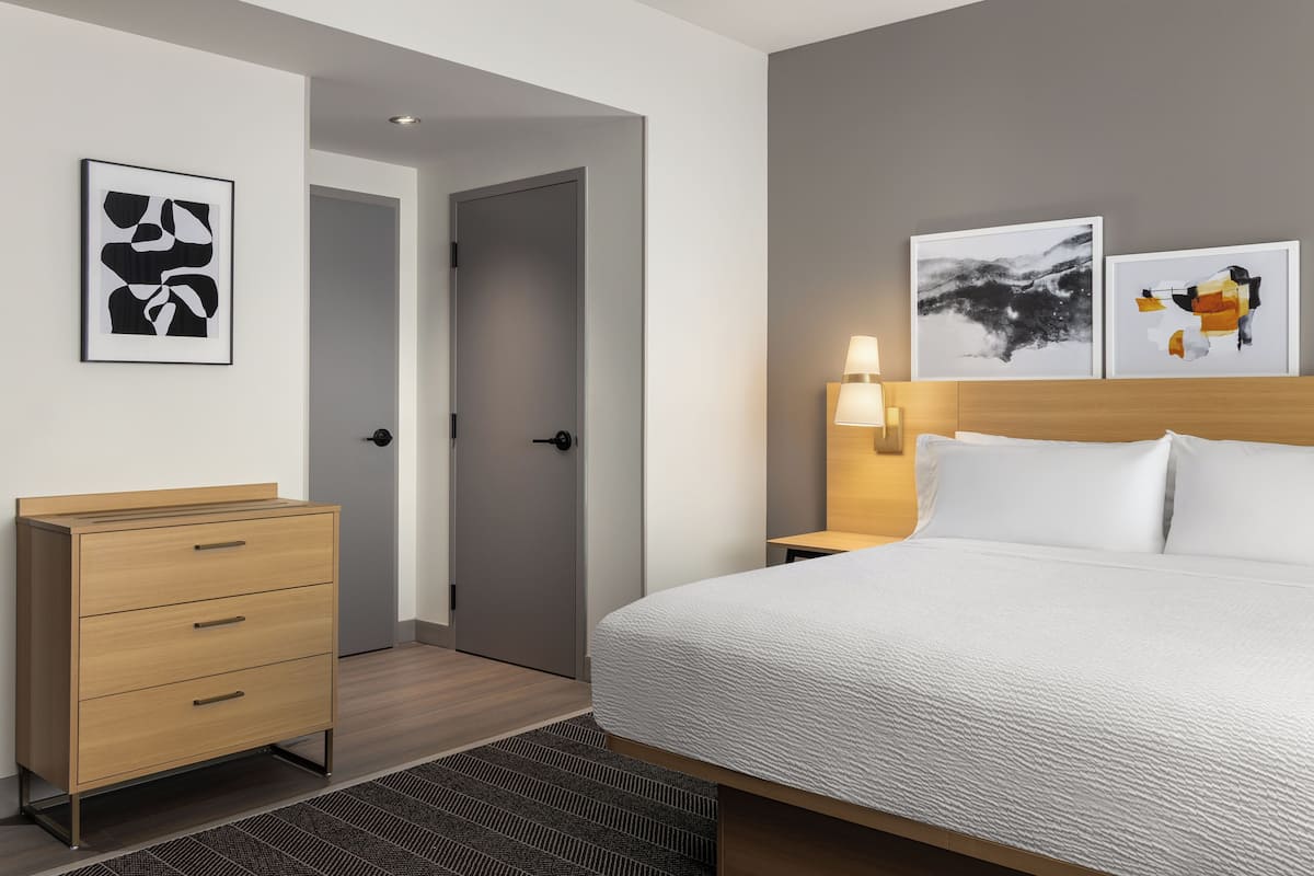 Ein Hotelzimmer mit einem Bett, einem Schminktisch, einer Tür und zwei an der Wand befestigten Kunstwerken.