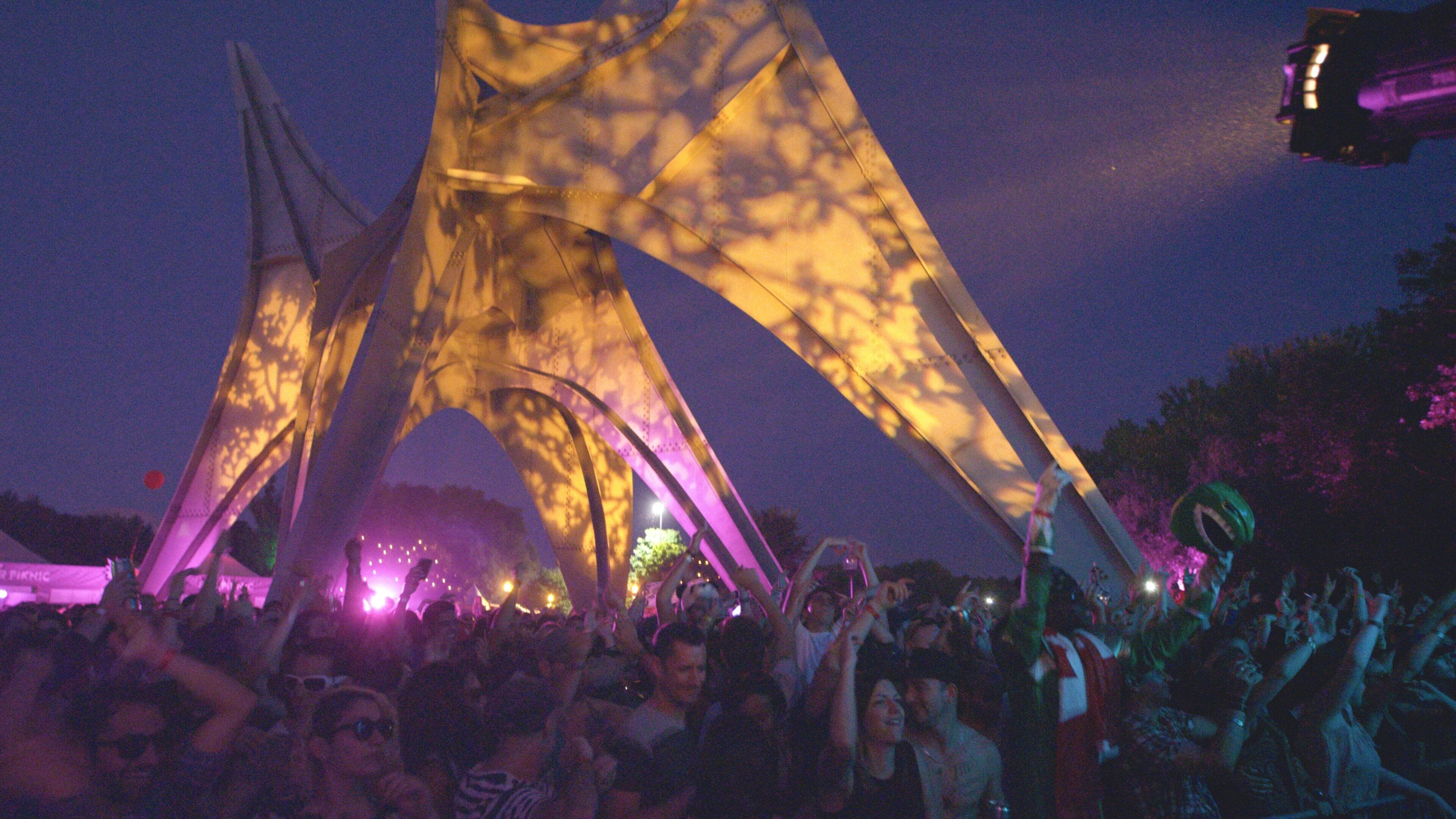 Una multitud de personas en un evento al aire libre, con una estructura iluminada grande al fondo.