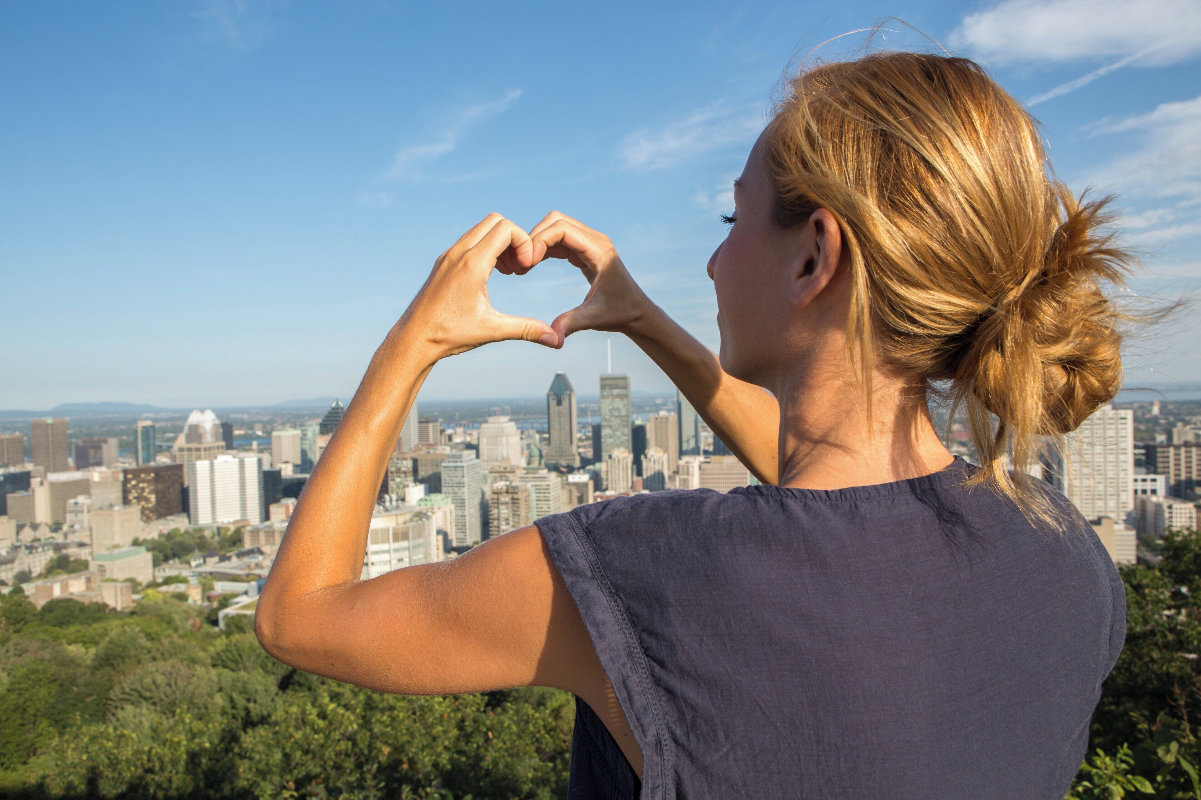 Una persona forma un corazón con las manos, observando un paisaje urbano con varios edificios.