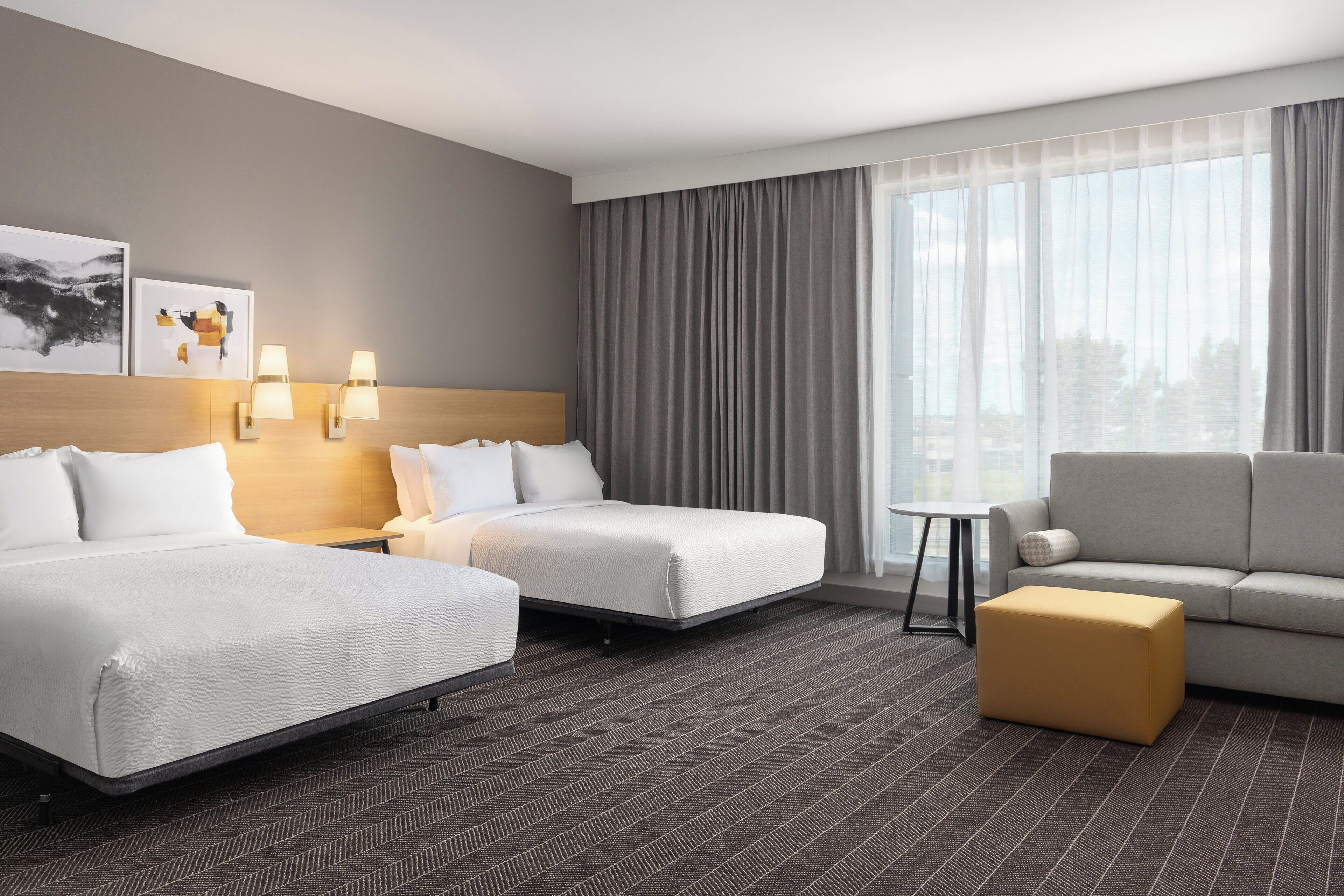 Habitación de hotel con dos camas, un sofá, una mesita y una ventana con cortinas.