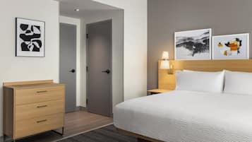 A hotel room with a bed, a wooden dresser, a door, and two wall-mounted artworks.