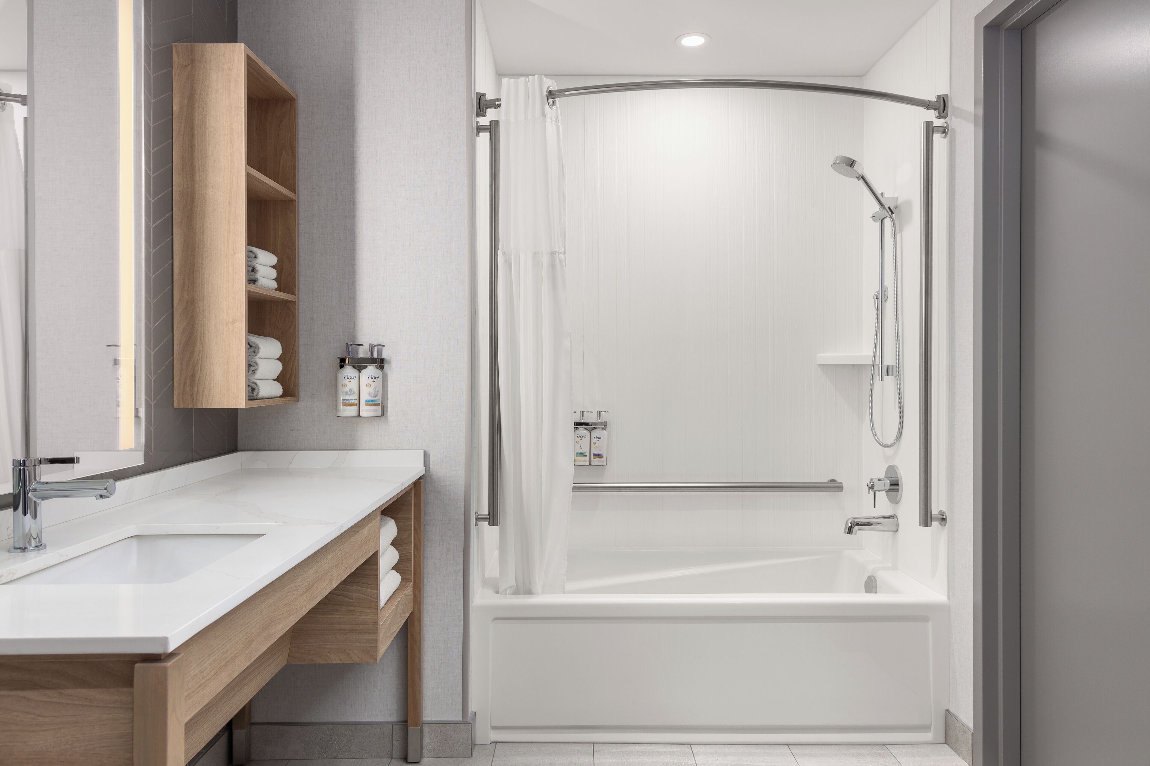 A modern bathroom with a white bathtub, a wooden vanity with a mirror, and a shower area with a glass door.