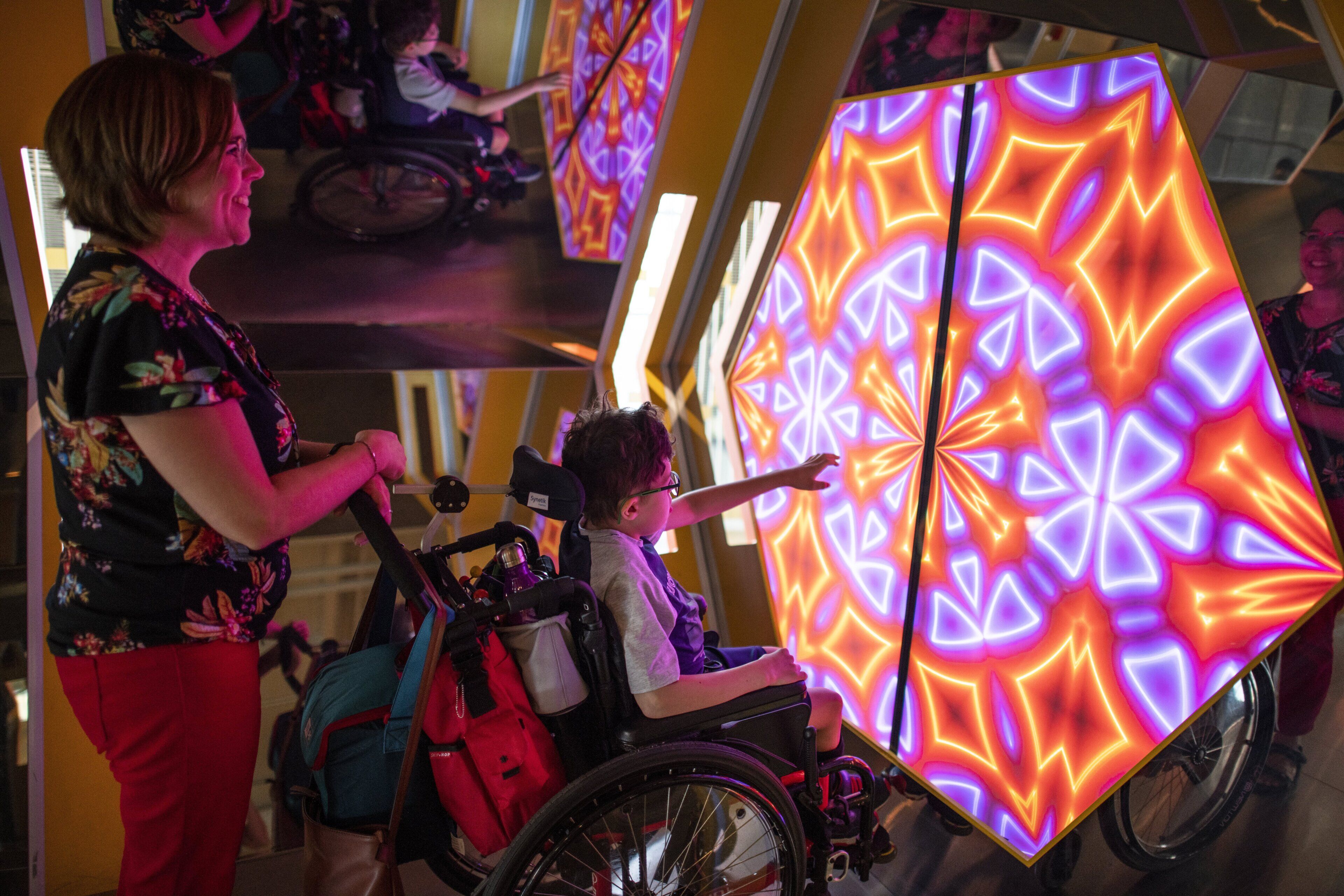 A person in a wheelchair interacting with a large, illuminated geometric structure.