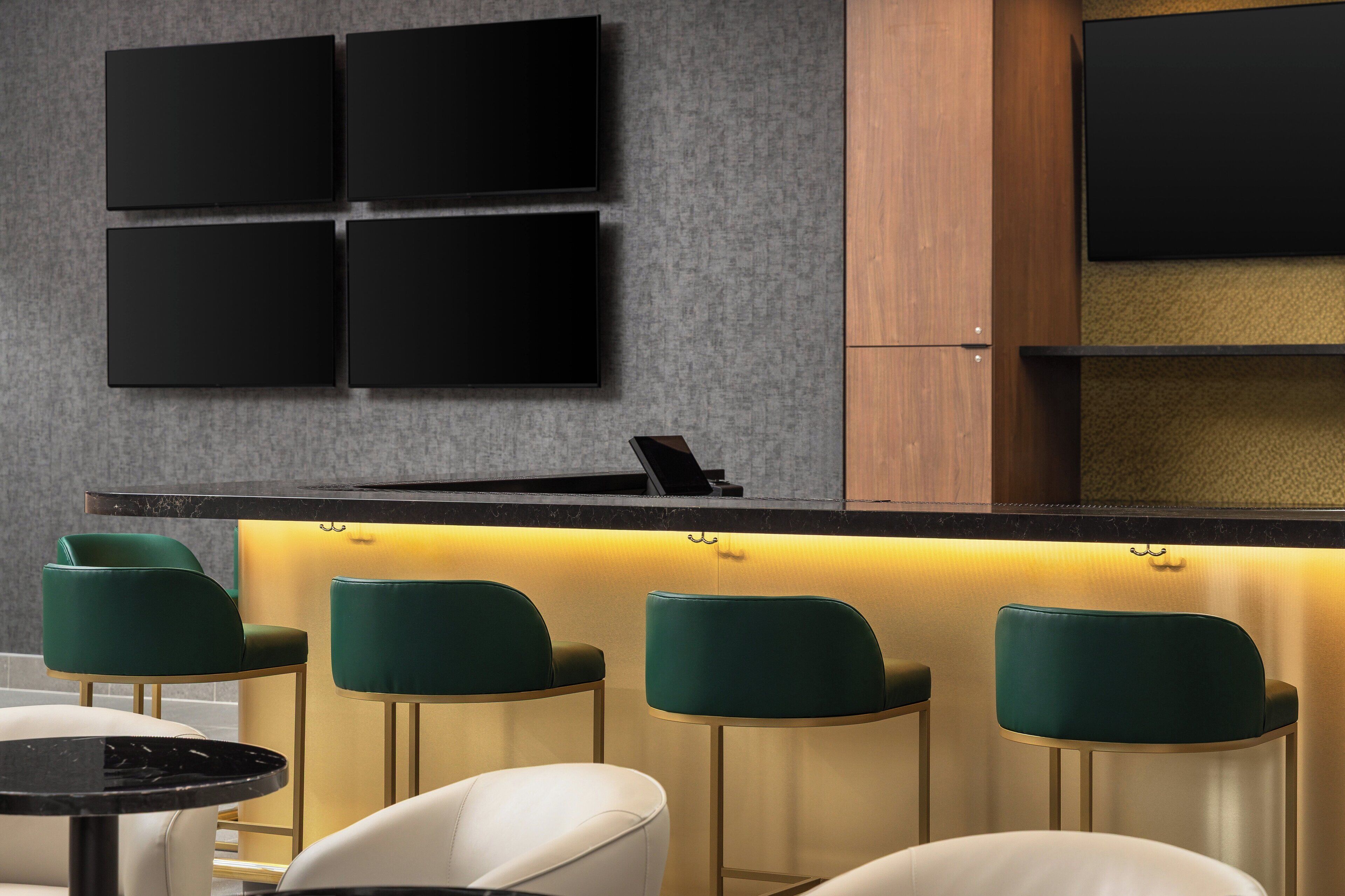 A bar area with a counter, bar stools, and wall-mounted TVs.