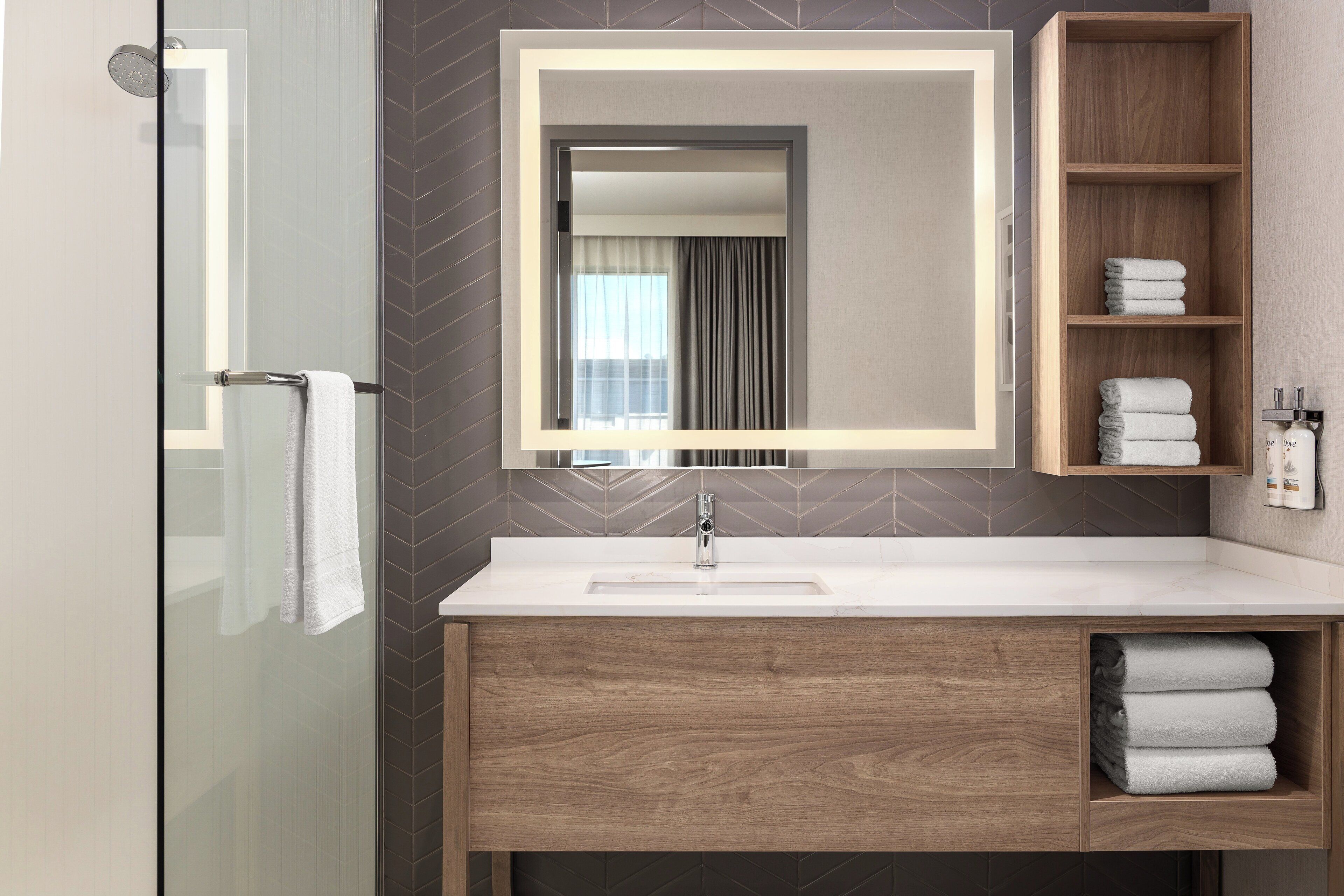 Een moderne badkamer met een douchecabine van glas, een houten wastafelmeubel met spiegel en een handdoekrek.