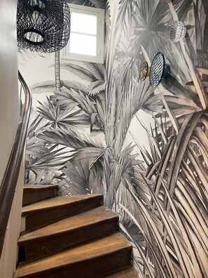 A staircase with wooden steps and a wall mural of tropical foliage. - Charming attic studio (Paris)