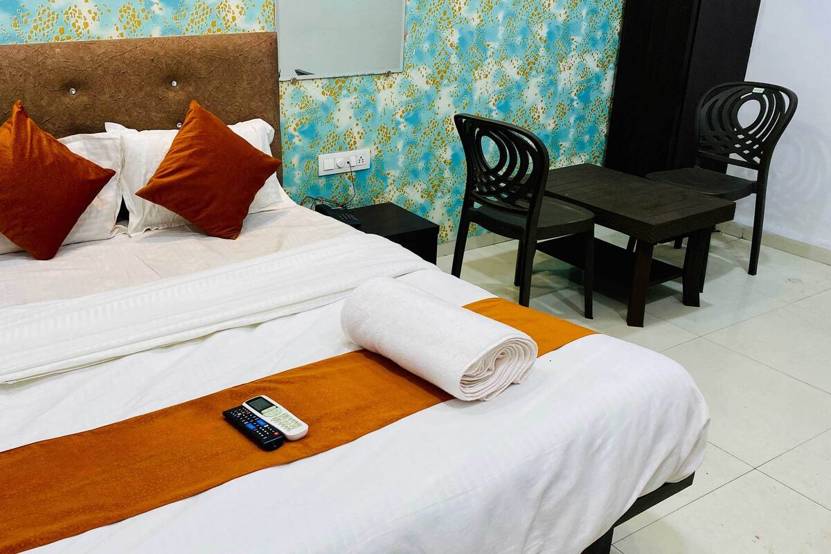 A neatly made bed with white and brown bedding, a remote control, and a rolled towel on the bed.