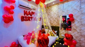 A room with a bed, red balloons, and a 'Happy Birthday' sign.