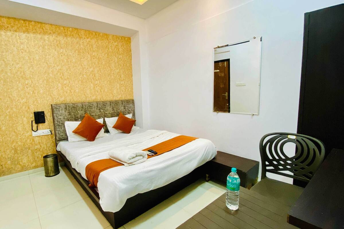 A hotel room with a bed, a chair, a water bottle, and a trash bin.