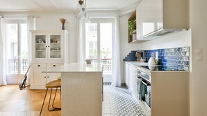 A modern kitchen with white cabinetry, a central island, and blue-tiled backsplash. - A Peaceful Retreat in Le Marais (Paris)