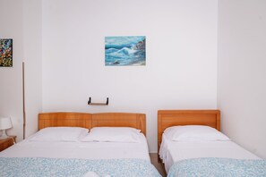 A hotel room with two beds, a painting of a seascape, a wooden headboard, and a bedside table with a lamp.