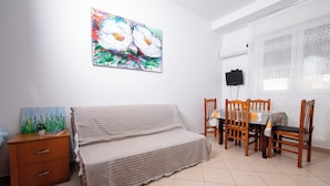 Ein Zimmer mit einer Couch, einem Esstisch mit Stühlen, einem Fernseher und einem Bild an der Wand.