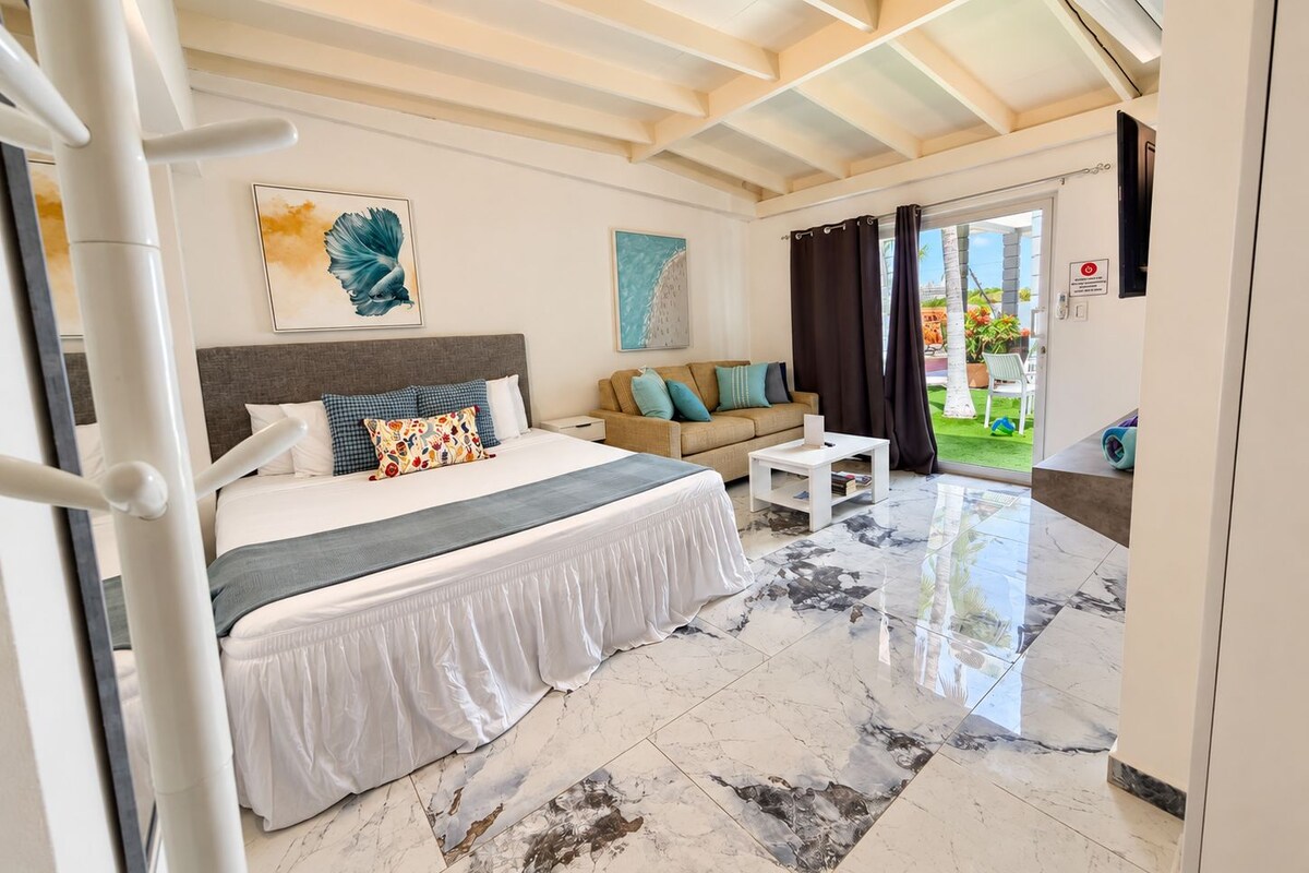A hotel room with a bed, a sofa, a coffee table, and a view of the outdoors.