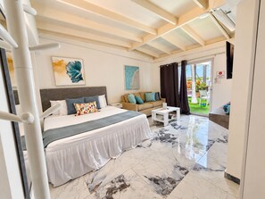 A hotel room with a bed, a sofa, a coffee table, and a view of the outdoors. - Homey Vacation Retreat (Noord)