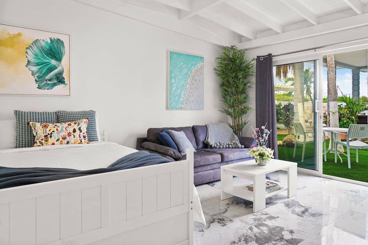 Een moderne slaapkamer met een bed, een bank, een salontafel en een groot raam met uitzicht op een tuin.
