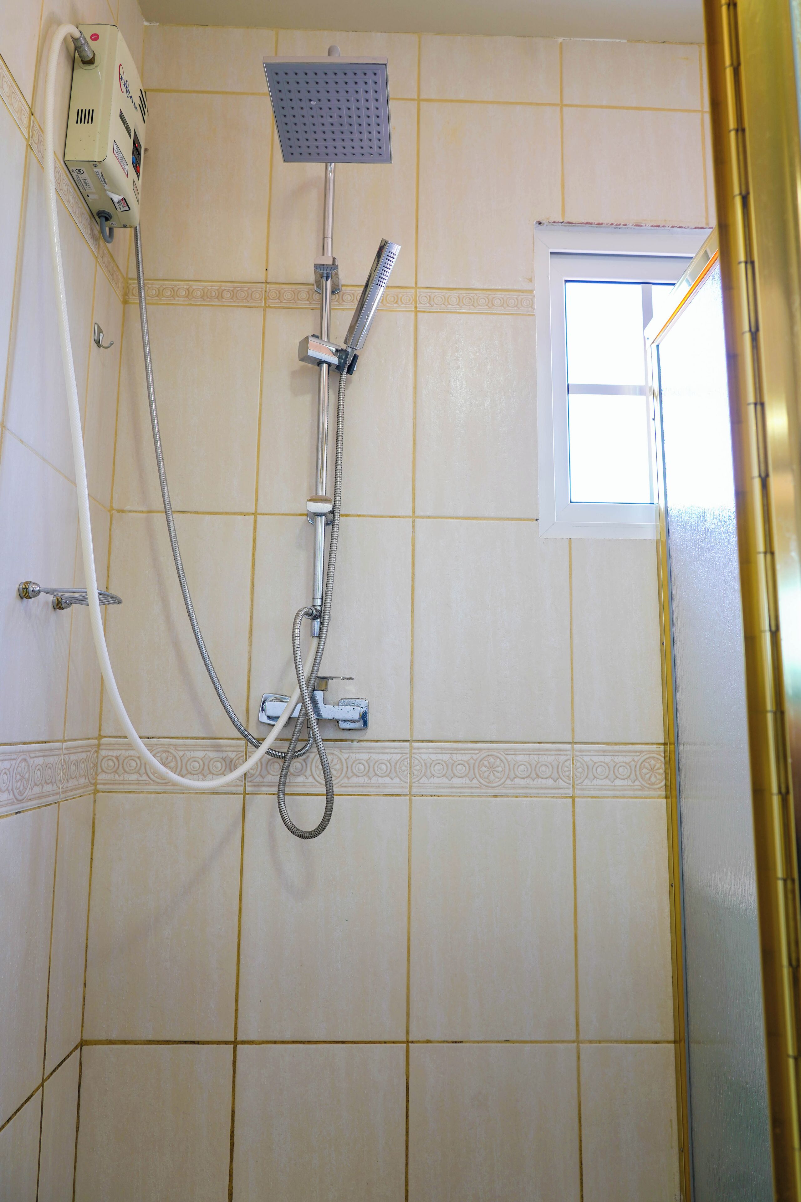 A shower with a handheld showerhead and a wall-mounted showerhead, connected to a wall-mounted control panel.