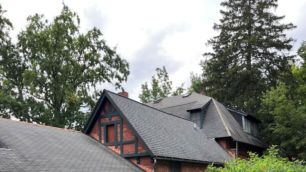 A brick house with a sloped roof, a garden with green grass and flower beds, and a barbecue grill.