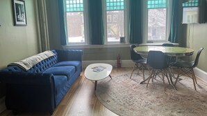 A living room with a blue sofa, a round coffee table, and a dining table with chairs.