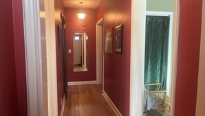 A hallway with red walls, a wooden floor, and a mirror on the wall.