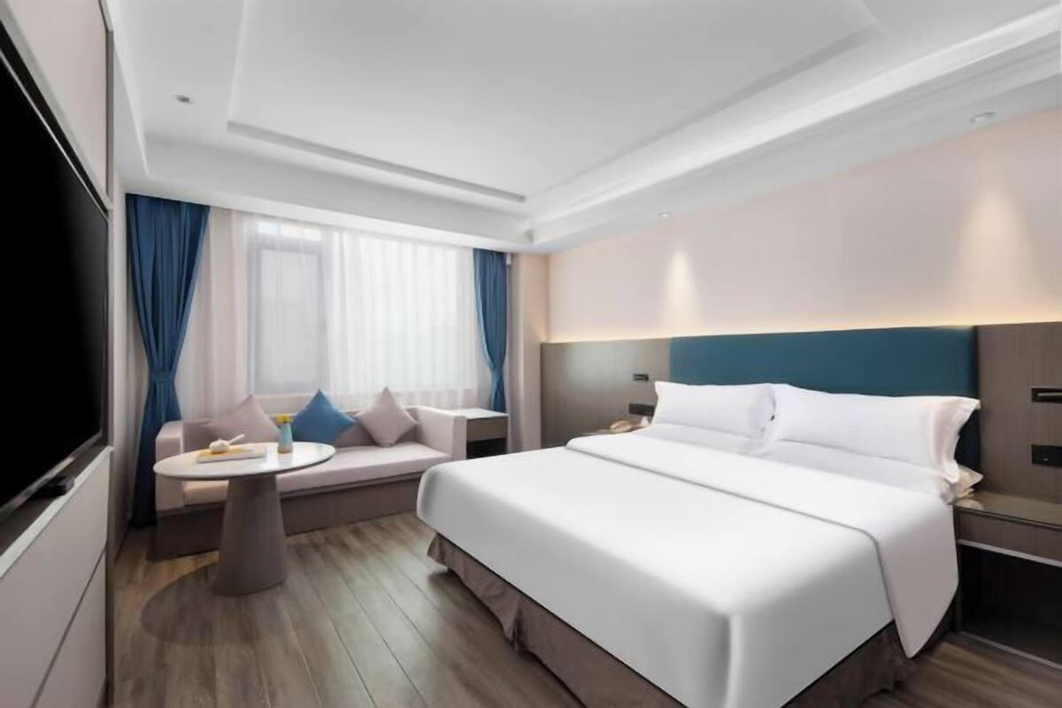 Una habitación de hotel moderna con una cama grande, un sofá, una mesita redonda y un televisor.